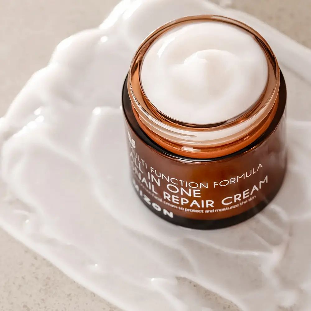 Geöffnete braune Glasdose mit Creme. Aufschrift: All In One, Snail Repair Cream, Mizon. Creme auf weißem Untergrund.