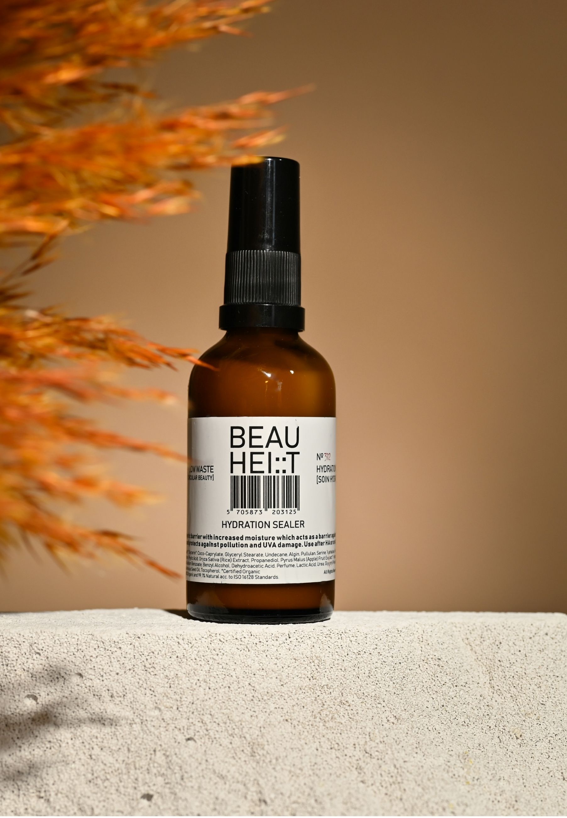 Braune Glasflasche mit schwarzem Sprühkopf. Weißes Etikett mit Produktnamen und Barcode. Hintergrund: beige und orangefarbene Elemente.