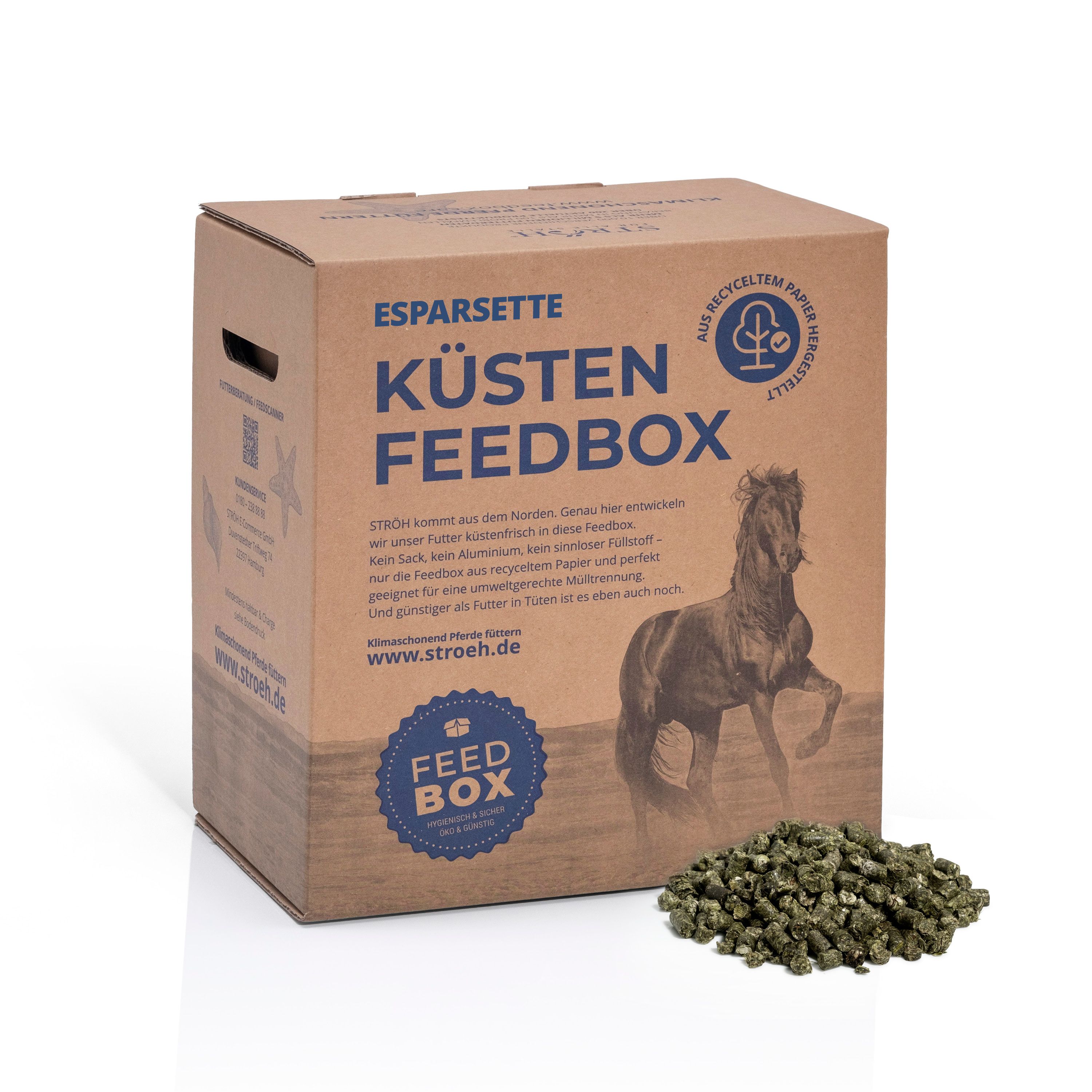 Karton Küsten Feedbox mit Esparsette-Cobs und Text. Auf recyceltem Papier. Logo: Baum. Cobs liegen vor der Box.