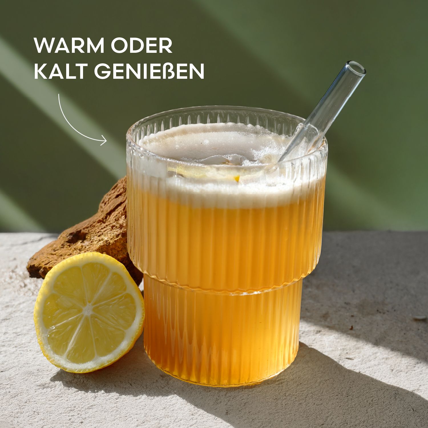 Glas mit Getränk und Strohhalm. Text: Warm oder kalt genießen. Eine halbe Zitrone liegt daneben.