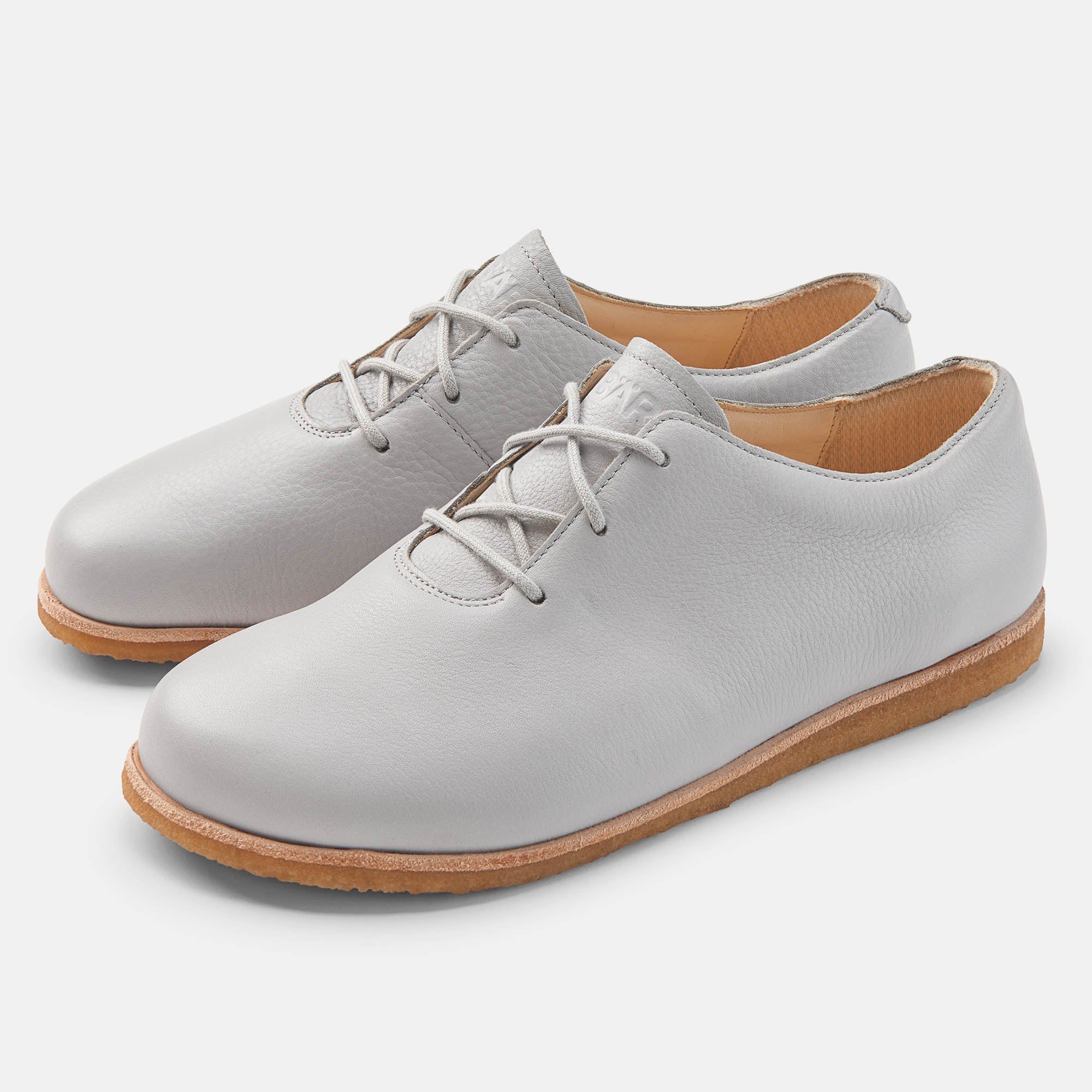 Hellgraue Lederschnürschuhe. Runde Zehen, helle Schnürsenkel, helle Sohle. Zwei Schuhe nebeneinander.