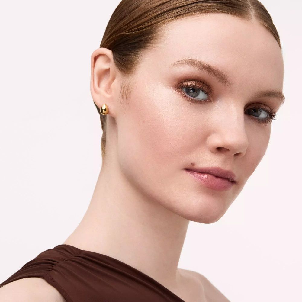 Porträt einer Frau mit braunem Lidschatten. Sie trägt ein braunes Oberteil und hat einen hellen Teint.