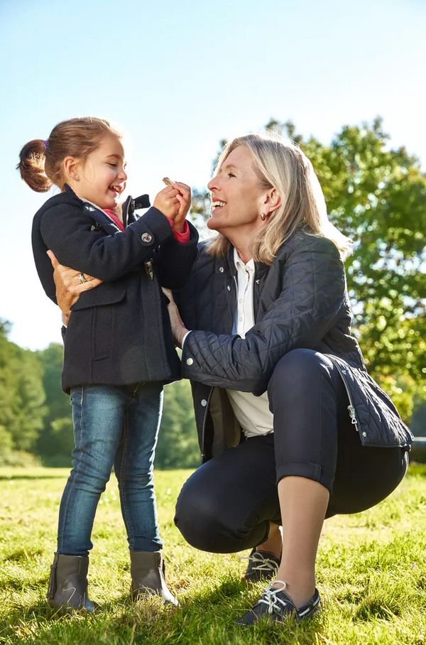 Frau und Kind im Freien. Frau kniet, Kind steht. Beide lächeln sich an.