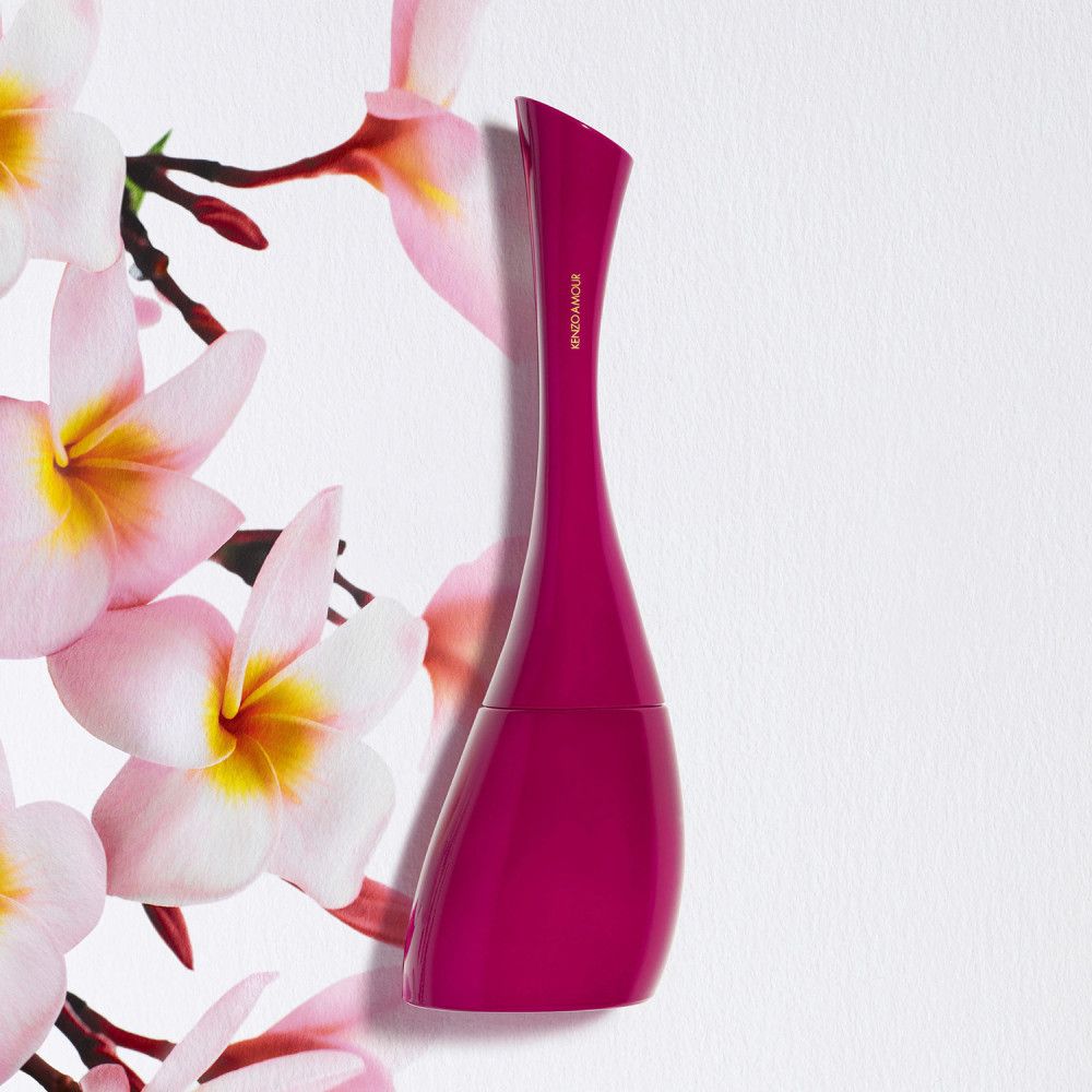 Pinkfarbener Flakon von Kenzo Amour. Geschwungene Form, vor Blüten platziert. Hintergrund weiß.