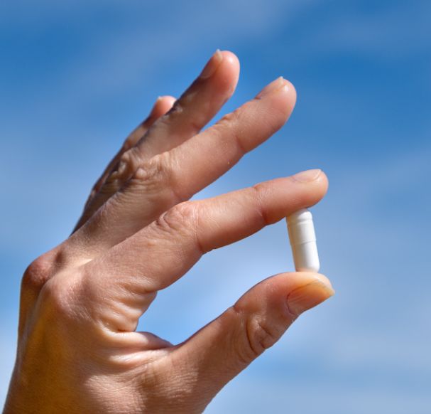 Hand hält eine weiße Kapsel des Aavalabs Magnesium Komplex.