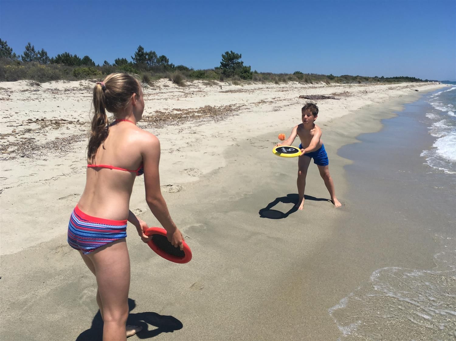 Zwei Kinder spielen am Strand mit Ogo Sport® Scheiben. Ein Kind wirft, das andere fängt.