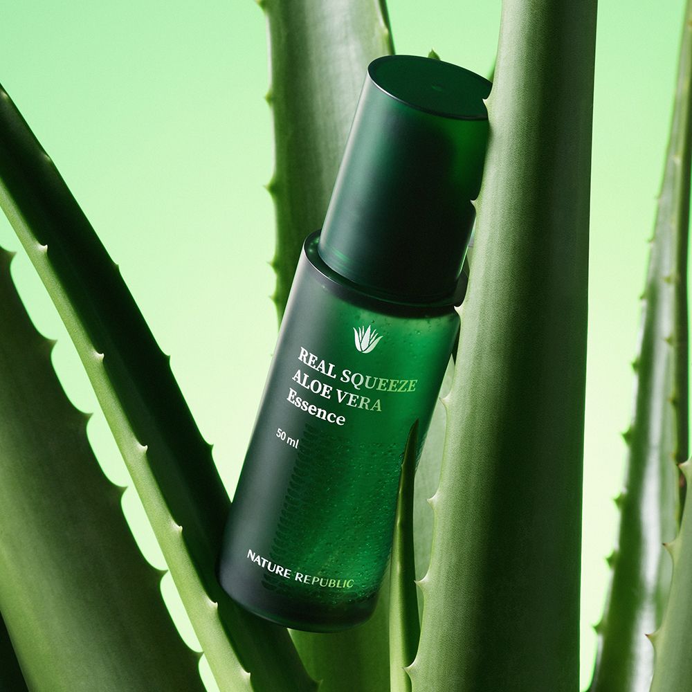 Grüne Flasche mit "REAL SQUEEZE ALOE VERA Essence" auf Aloe-Blättern.