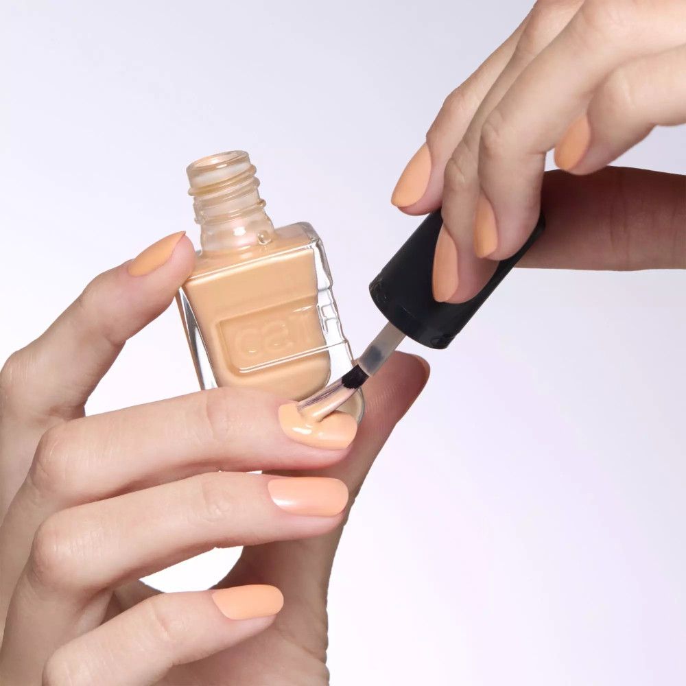 Hände lackieren Nägel mit Pinsel. Pfirsichfarbener Nagellack. Geöffnete Flasche.