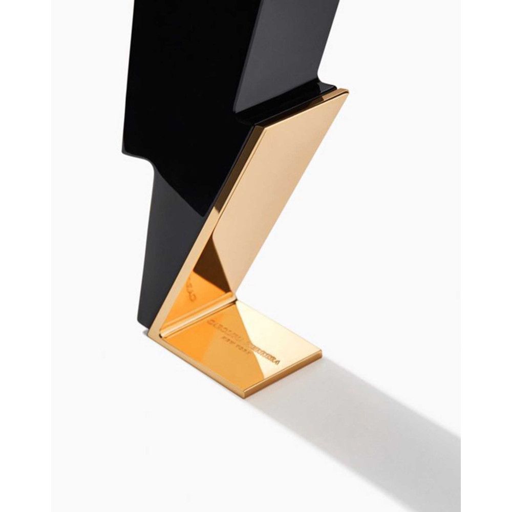 Schwarzer Flakon in Blitzform mit goldfarbenem Standfuß. Aufschrift auf dem Fuß.