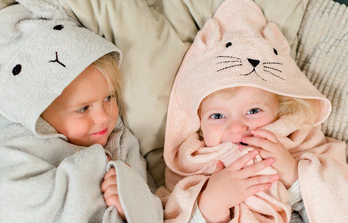 Zwei Kinder mit Kapuzenhandtüchern mit Katzenmotiven. Ein graues und ein rosa Handtuch.
