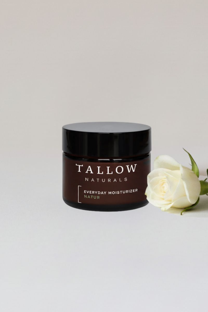 Braune Tiegel mit schwarzem Deckel. Aufschrift: TALLOW NATURALS, EVERYDAY MOISTURIZER NATUR. Daneben eine weiße Rose.