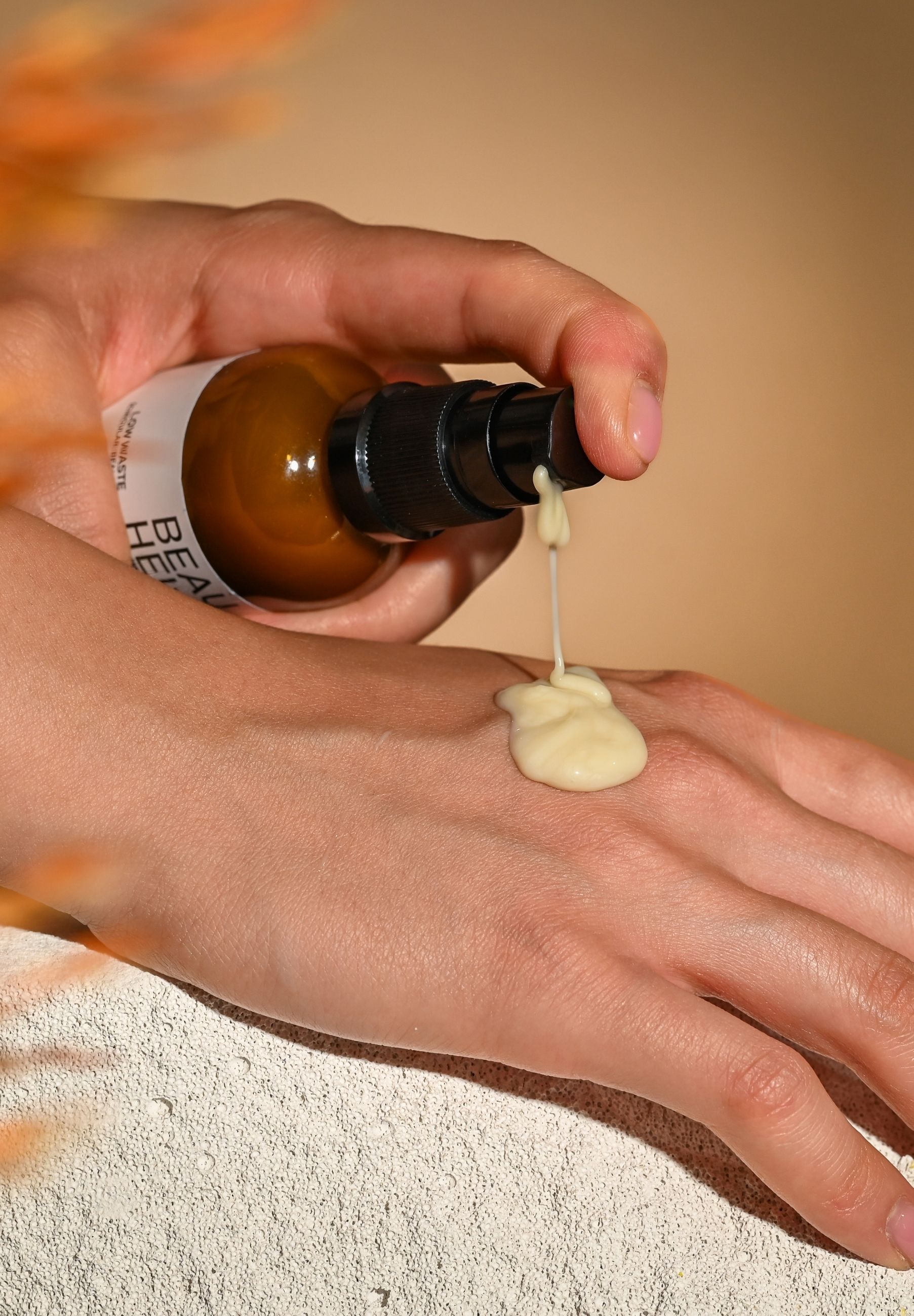 Hand drückt Serum aus einer braunen Flasche. Creme wird auf die Handfläche aufgetragen. BEAUHEIT-Etikett sichtbar.