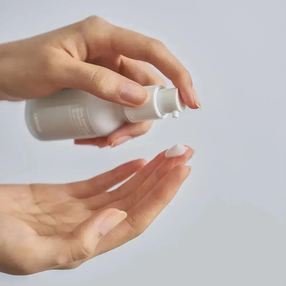 Hände halten eine weiße Flasche. Produkt wird auf die Hand aufgetragen.