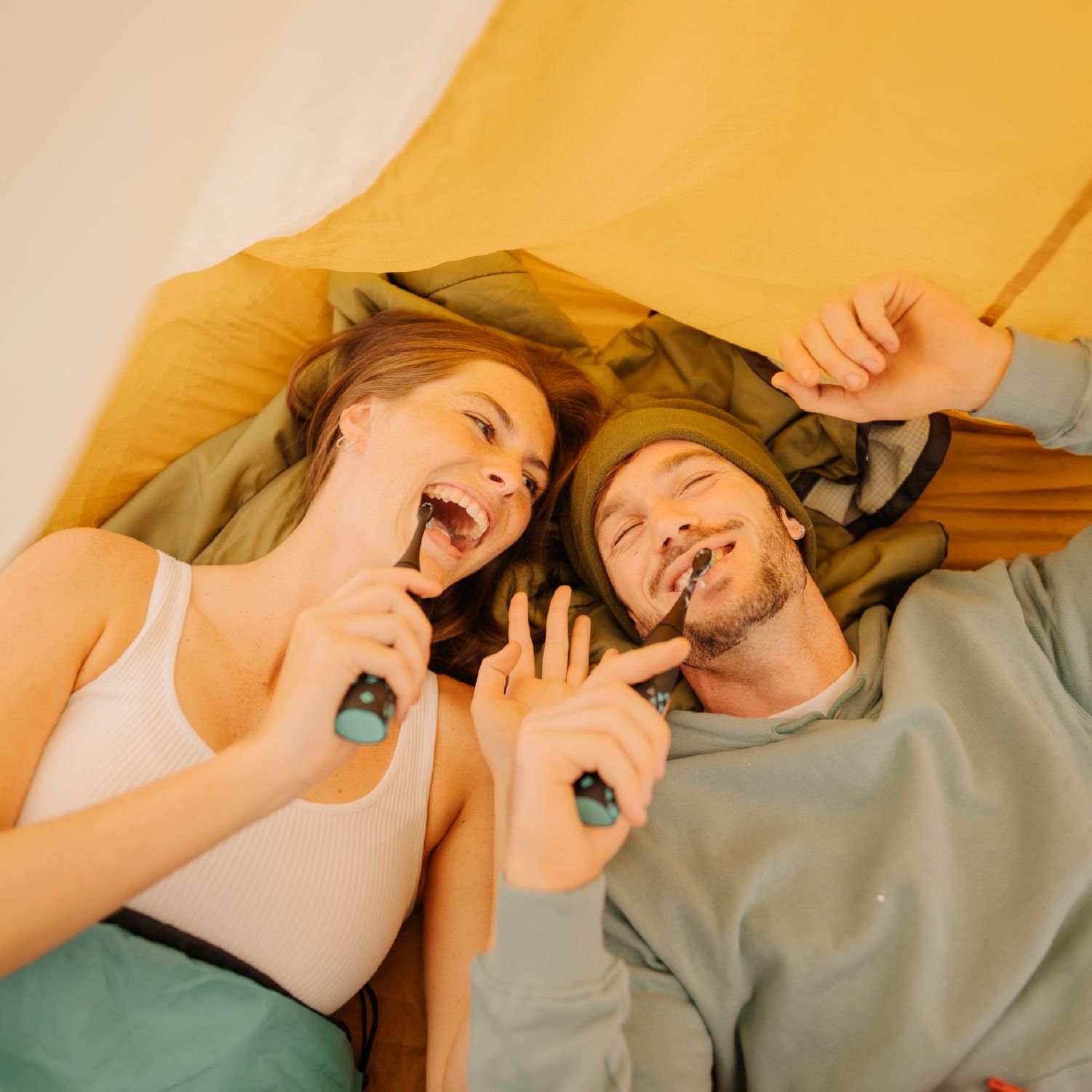 Zwei Personen lachen und putzen sich die Zähne mit schwarzen Zahnbürsten.