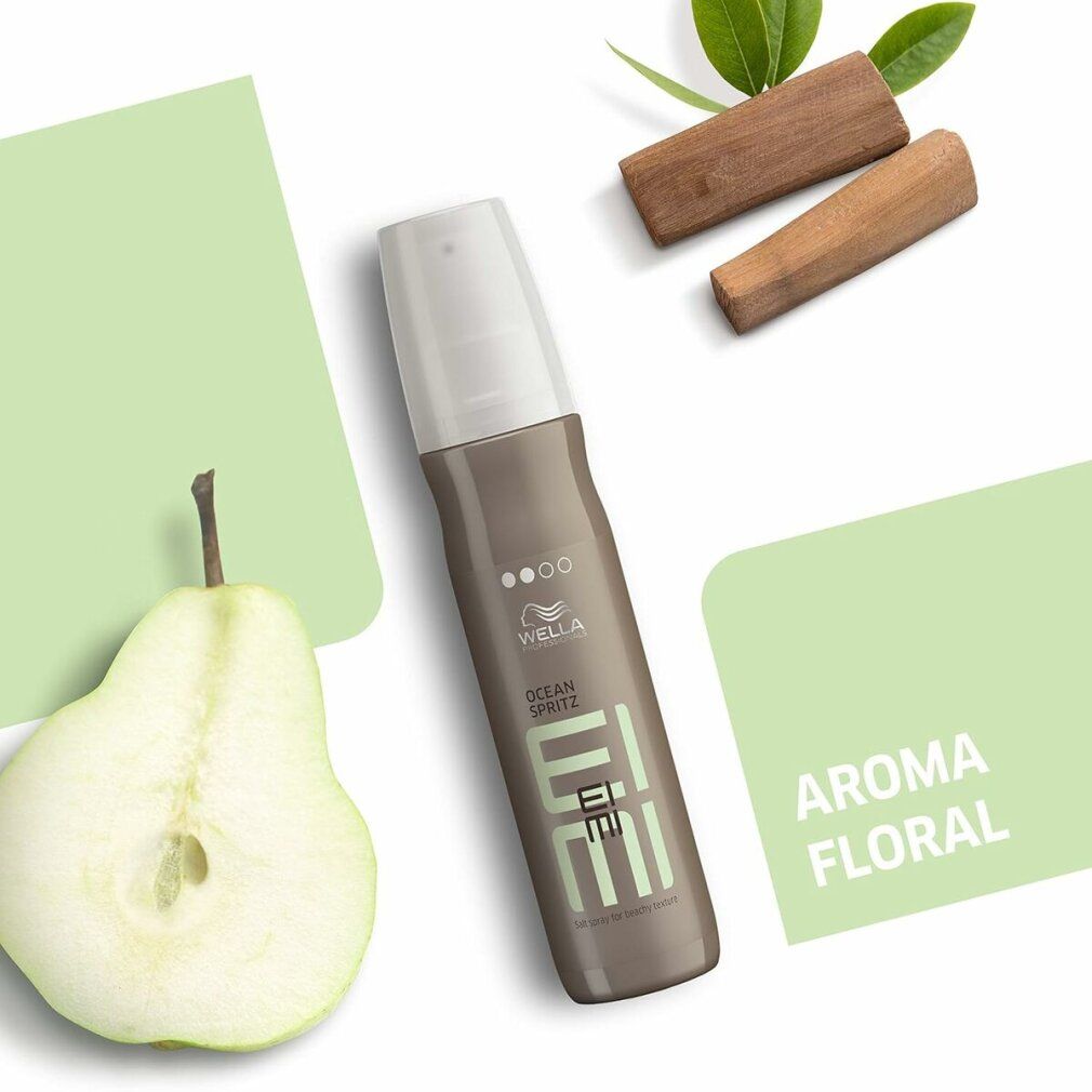 Styling-Spray-Flasche, umgeben von Birne, Holz und grünen Formen. Aufschrift: Wella EIMI Ocean Spritz, Aroma Floral.