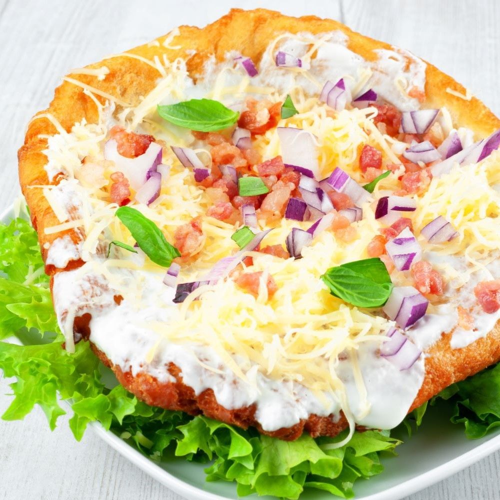 Gebratene Speise auf Salatbett. Mit Käse, Zwiebeln, Speck und Creme bedeckt.