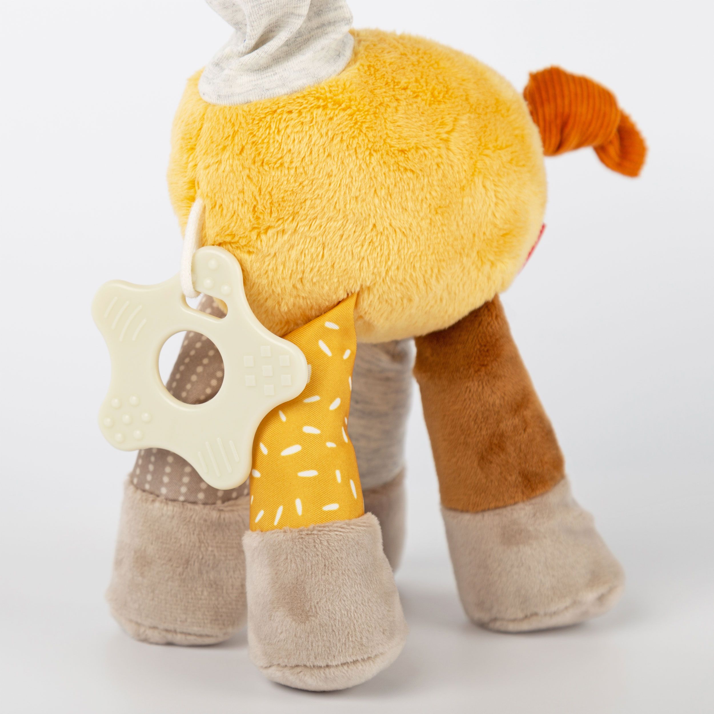 Nahaufnahme des Rückens einer gelben Stoffgiraffe. Stern-Beißring. Verschiedene Stoffe und Muster. Orangefarbener Schwanz.