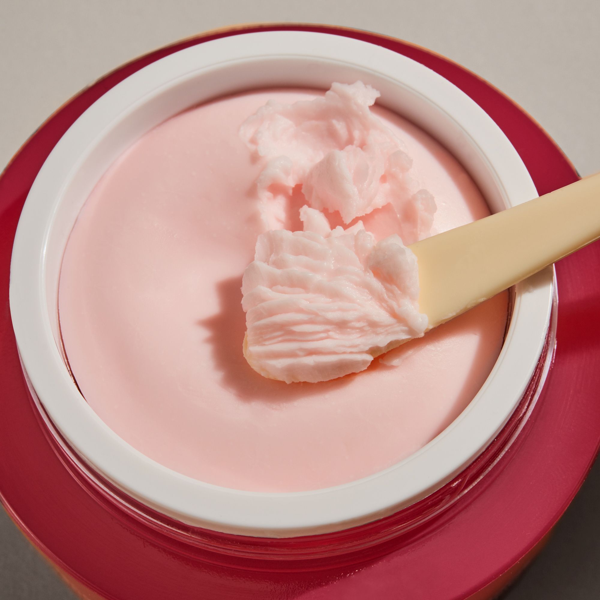 Geöffnete rosa Creme-Dose mit Creme und Spatel. Creme-Textur sichtbar.