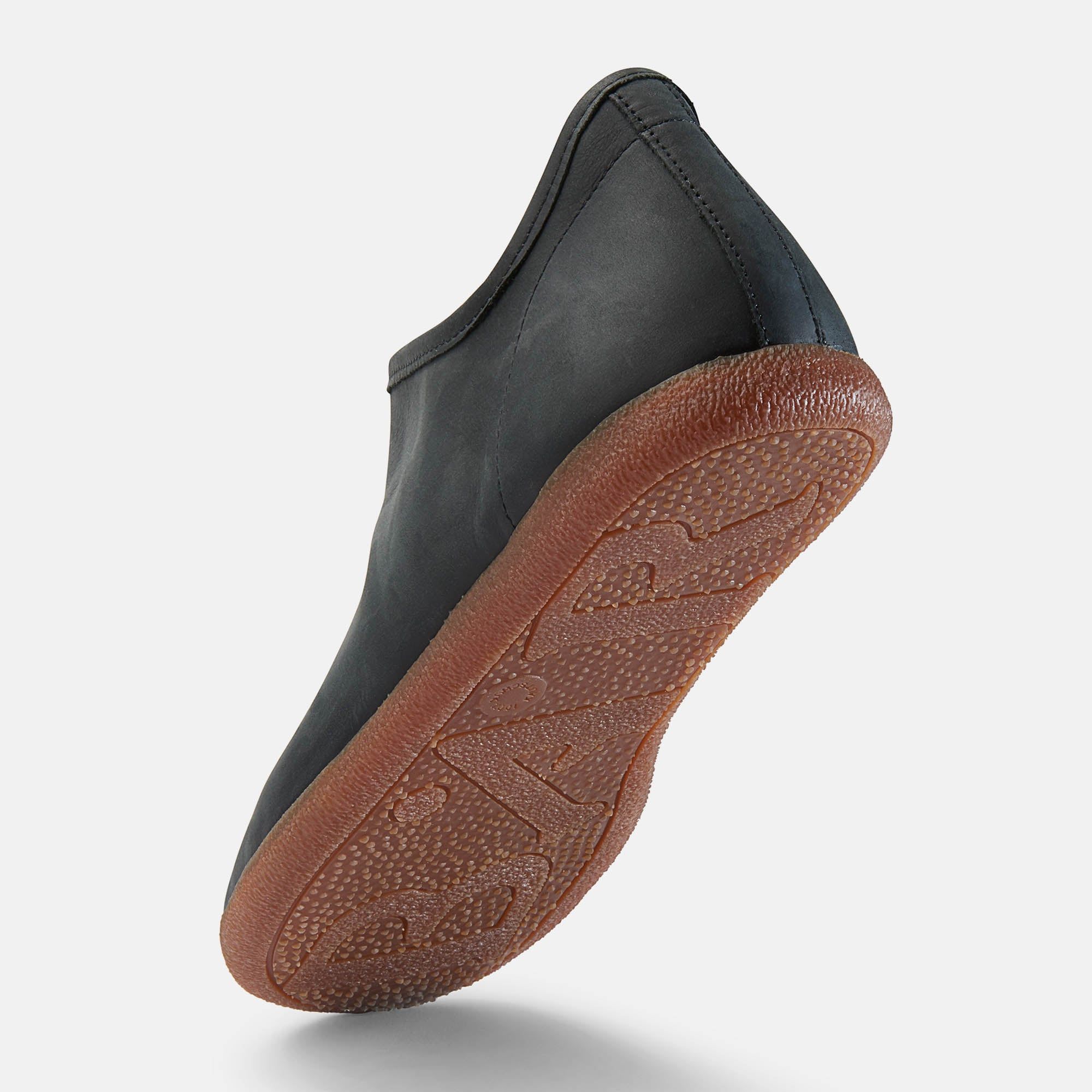 Schwarzer Slipper mit brauner Sohle. Sichtbare Sohle mit Muster. Perspektivische Ansicht.