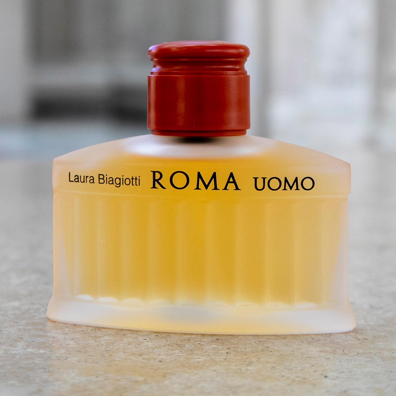 Parfümflakon mit gelblicher Flüssigkeit. Aufschrift: Laura Biagiotti ROMA UOMO. Auf grauem Hintergrund.