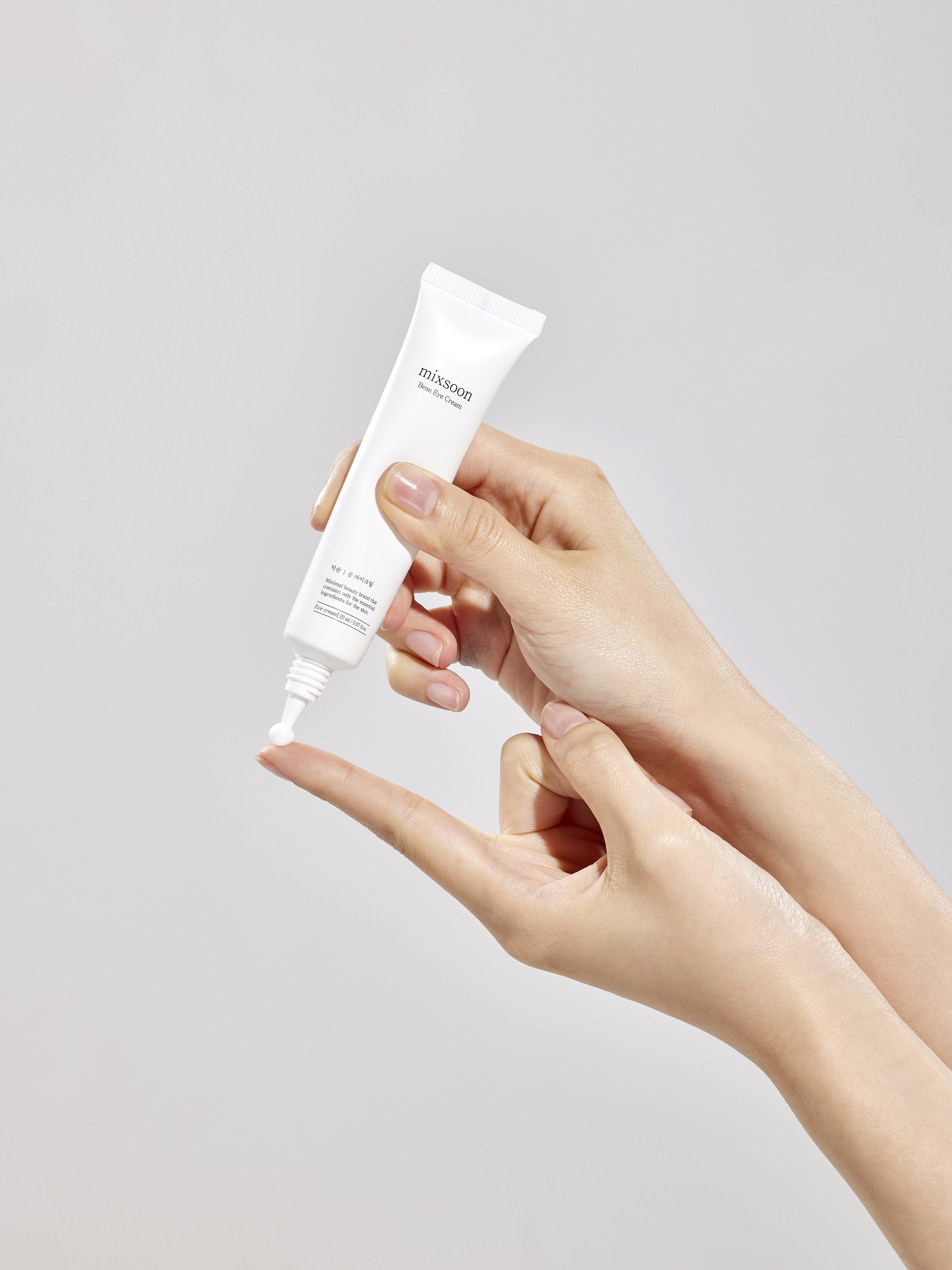 Hände halten Tube "mixsoon Bean Eye Cream". Creme auf Finger. Weißer Hintergrund.
