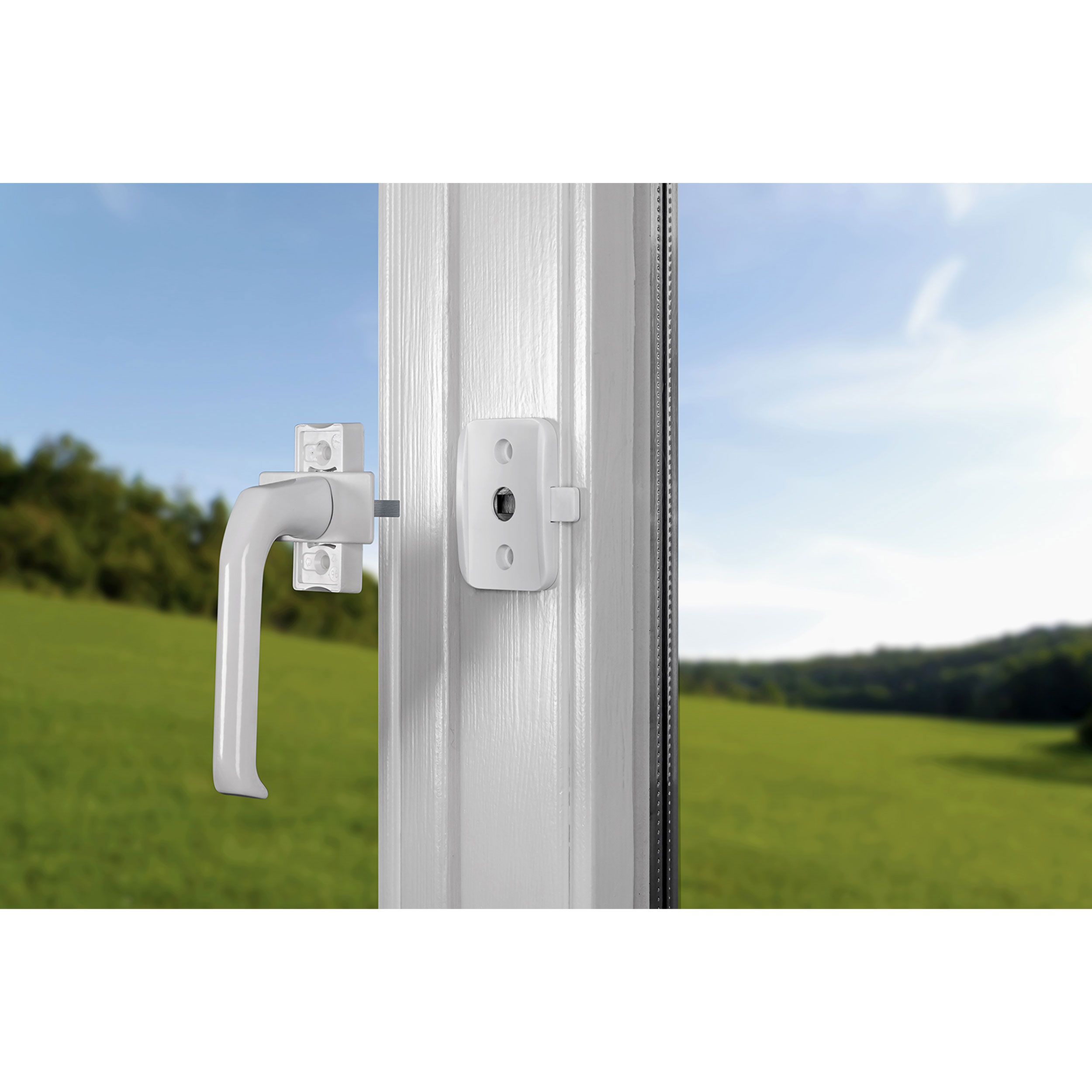 Fenstergriff mit weißer Sicherung. Hintergrund: Wiese und Himmel.