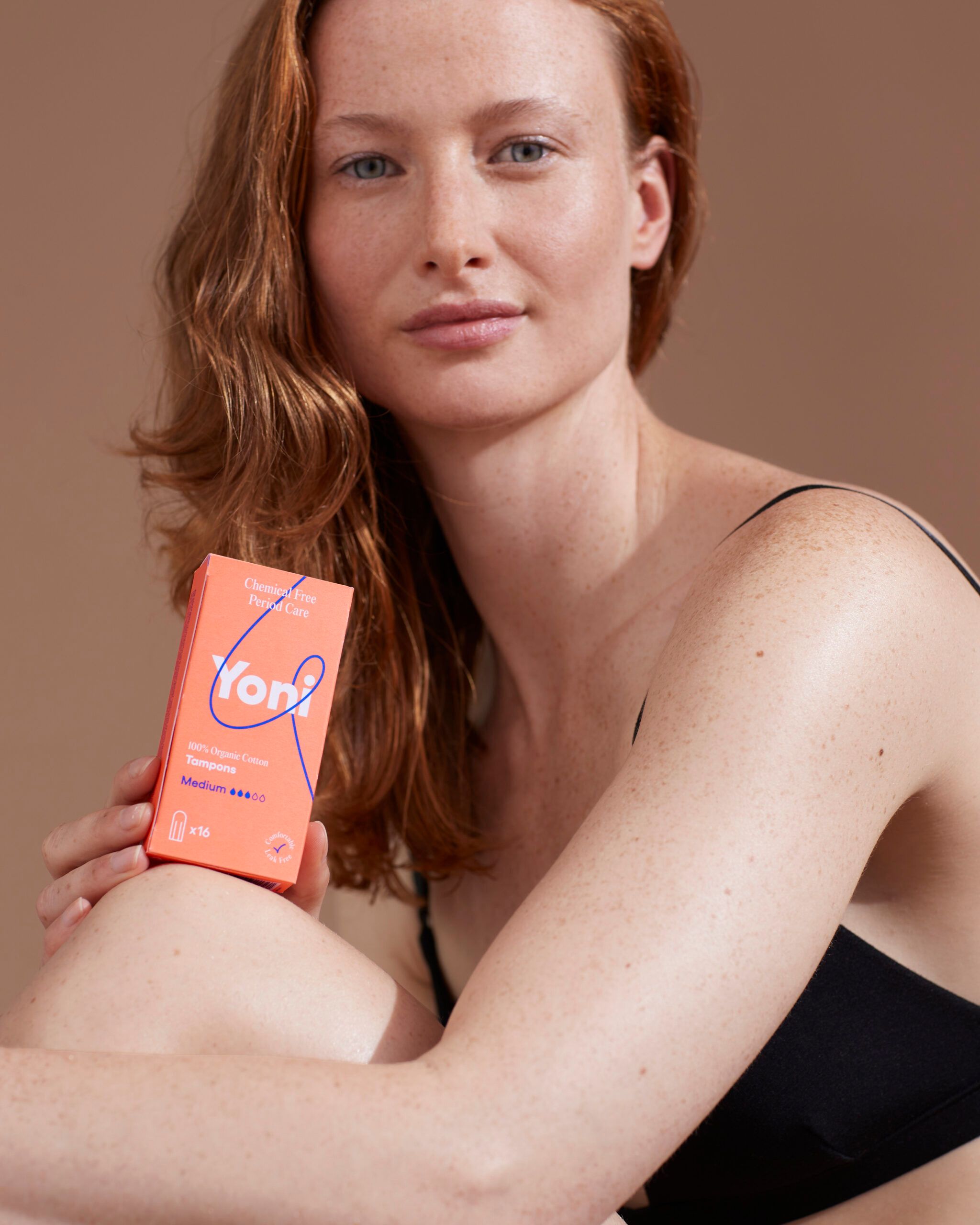 Eine Frau hält eine orangefarbene Schachtel mit Tampons. Auf der Schachtel steht "Yoni".