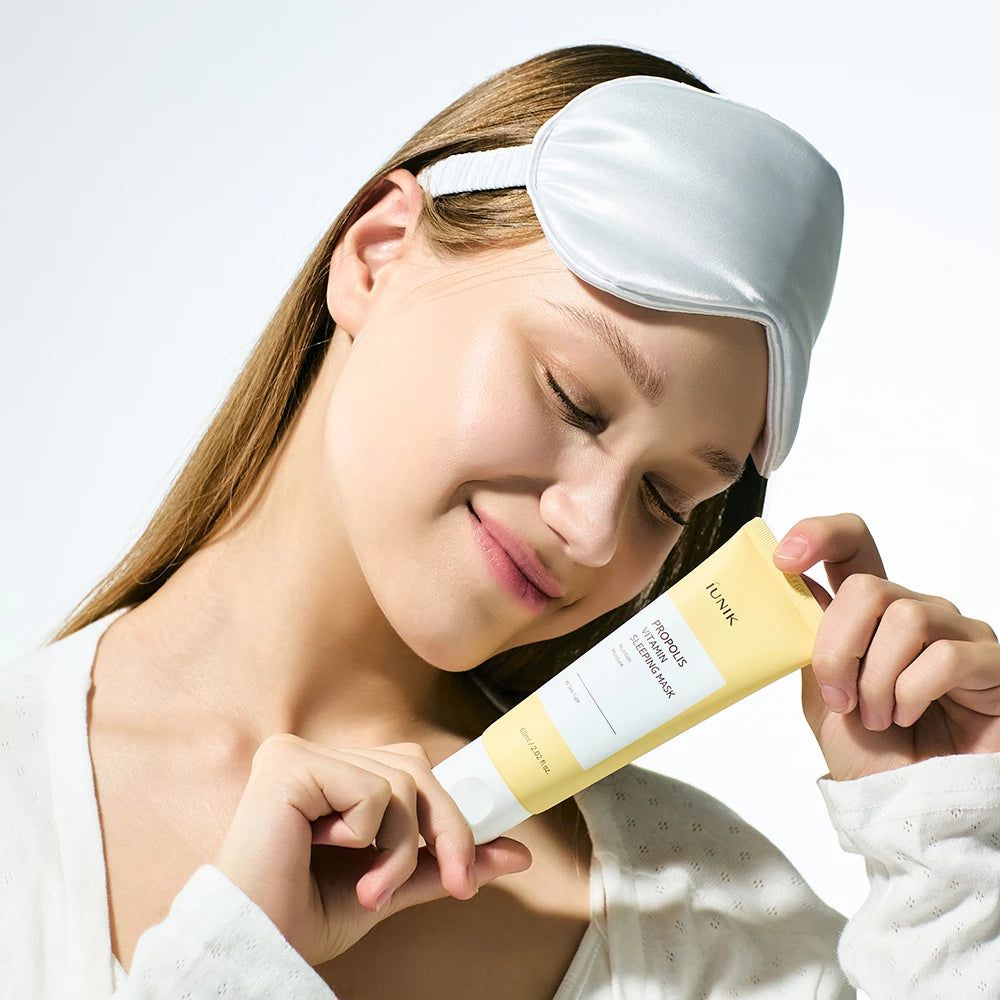 Frau mit Schlafmaske hält eine gelbe Tube Propolis Vitamin Sleeping Mask.