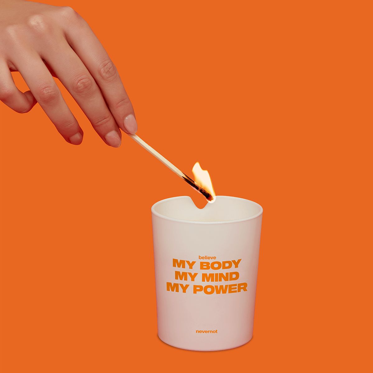 Weiße Kerze mit Text: believe, MY BODY MY MIND MY POWER. Eine Hand zündet die Kerze an.