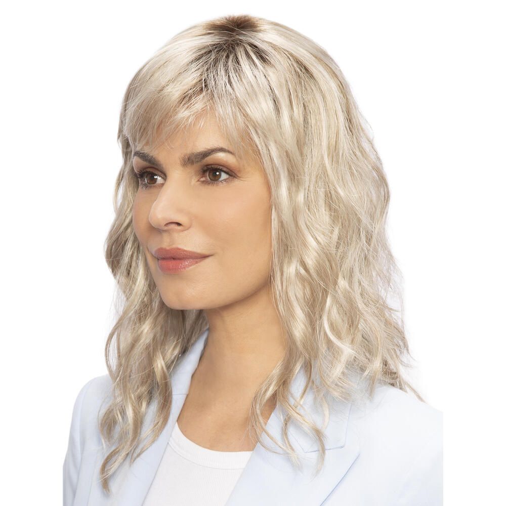 Perücke Kiky von trendhair. Blond, gewellt, mit Pony. Frau trägt hellblaues Jackett. Dreiviertelansicht.
