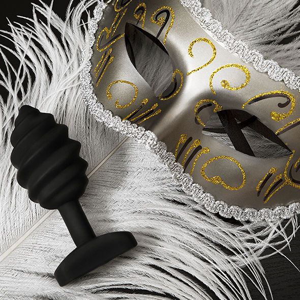 Schwarzer Plug mit spiralförmiger Form, neben einer Maske und Federn.