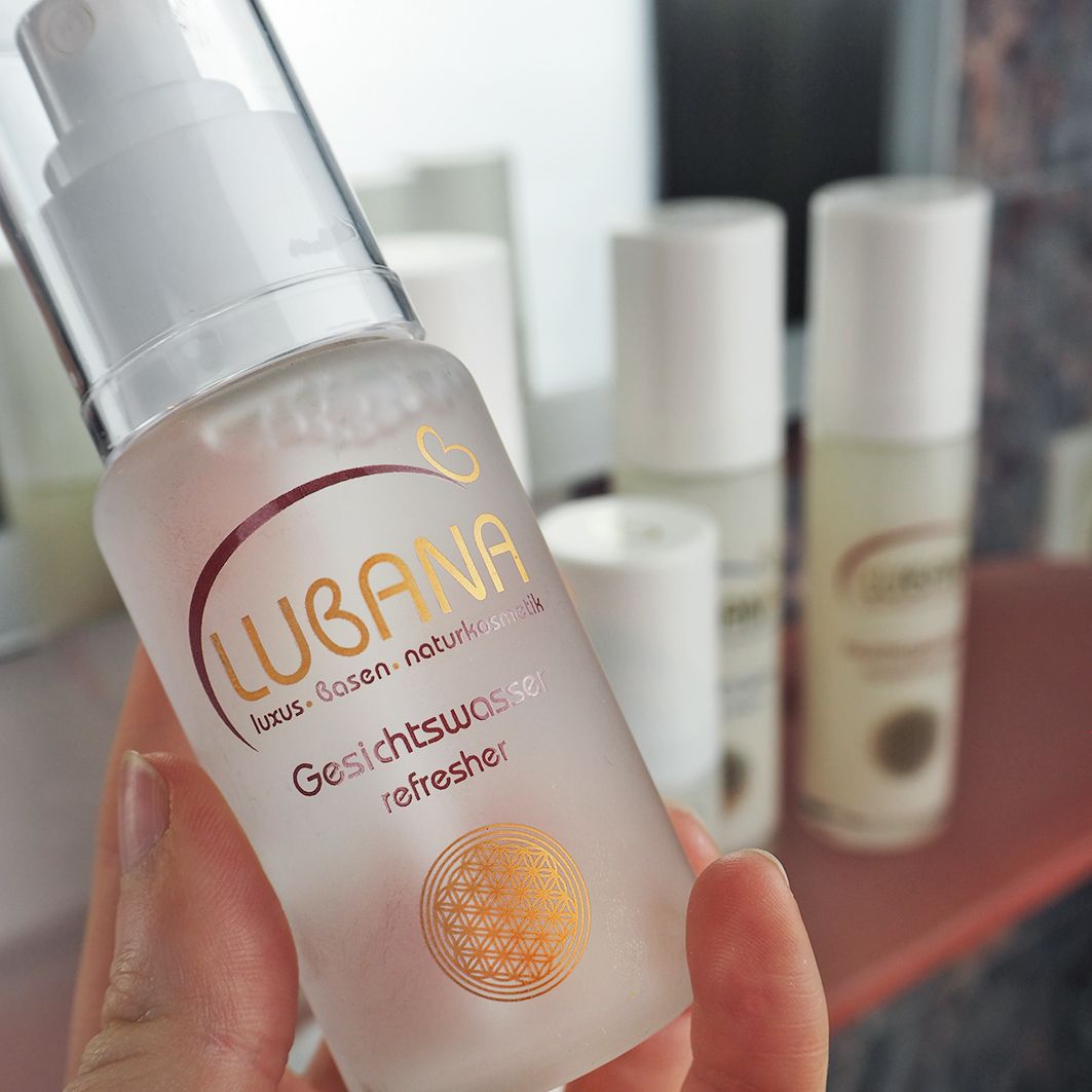 Hand hält Lubana Gesichtswasser Flasche. Aufschrift: Lubana, Gesichtswasser refresher. Weitere Flaschen im Hintergrund.