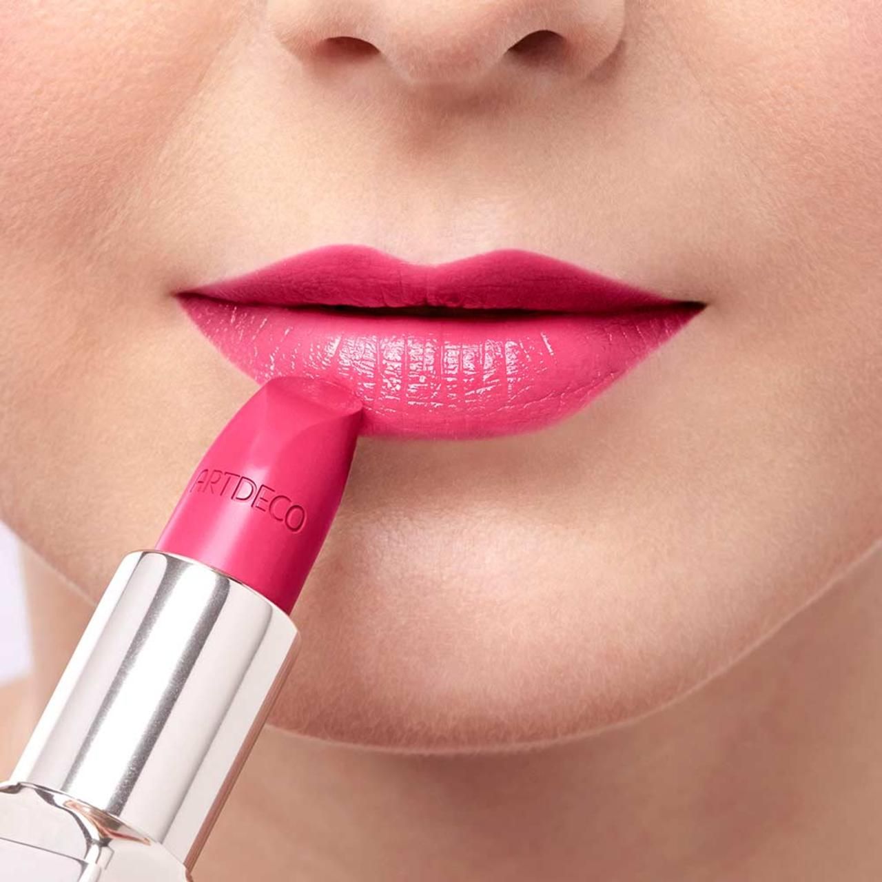 Person trägt pinken Lippenstift auf den Lippen auf. "ARTDECO" auf dem Lippenstift sichtbar.