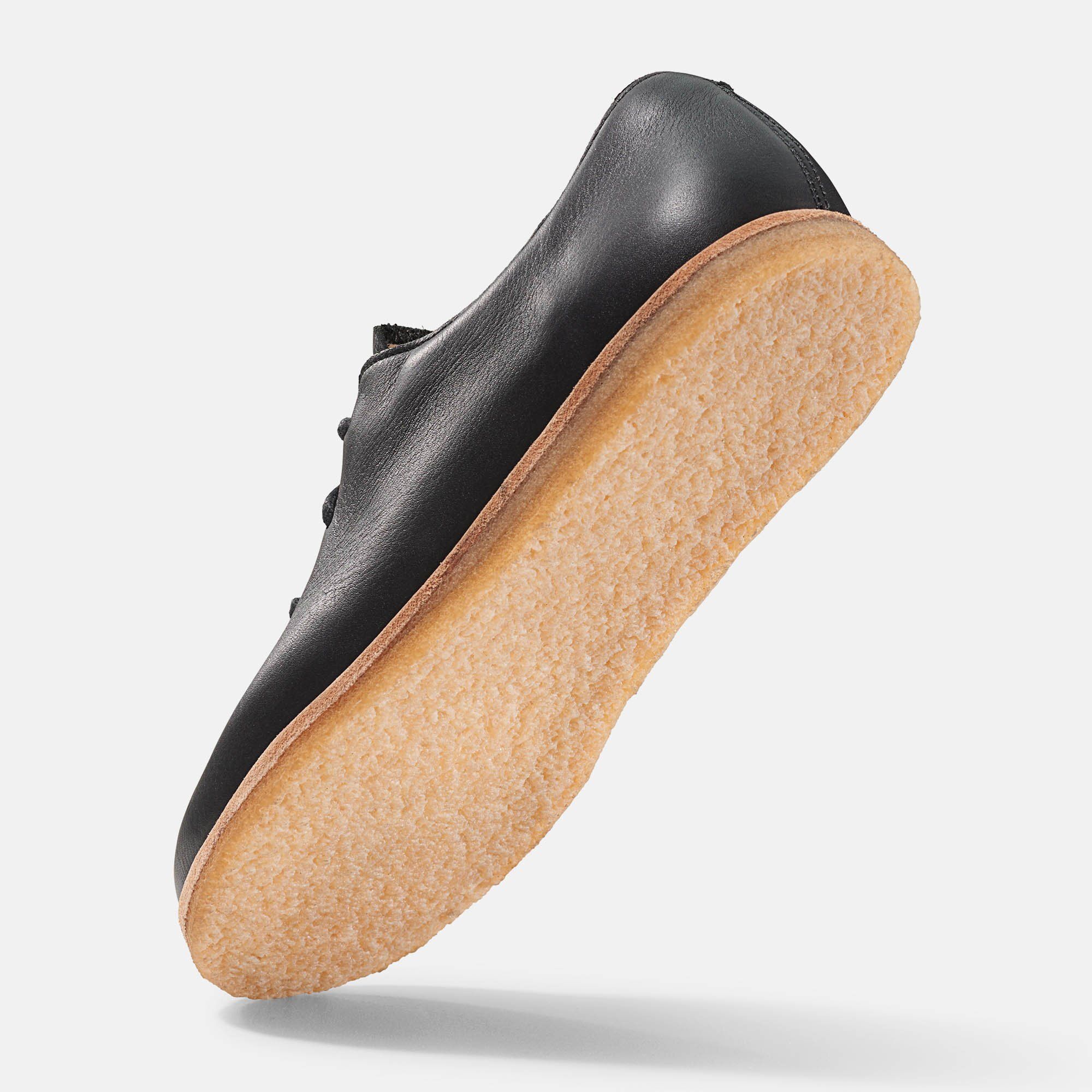 Schwarzer Lederschnürschuh, helle Sohle. Schuh von unten, leicht schräg. Sohle und Naht sichtbar.