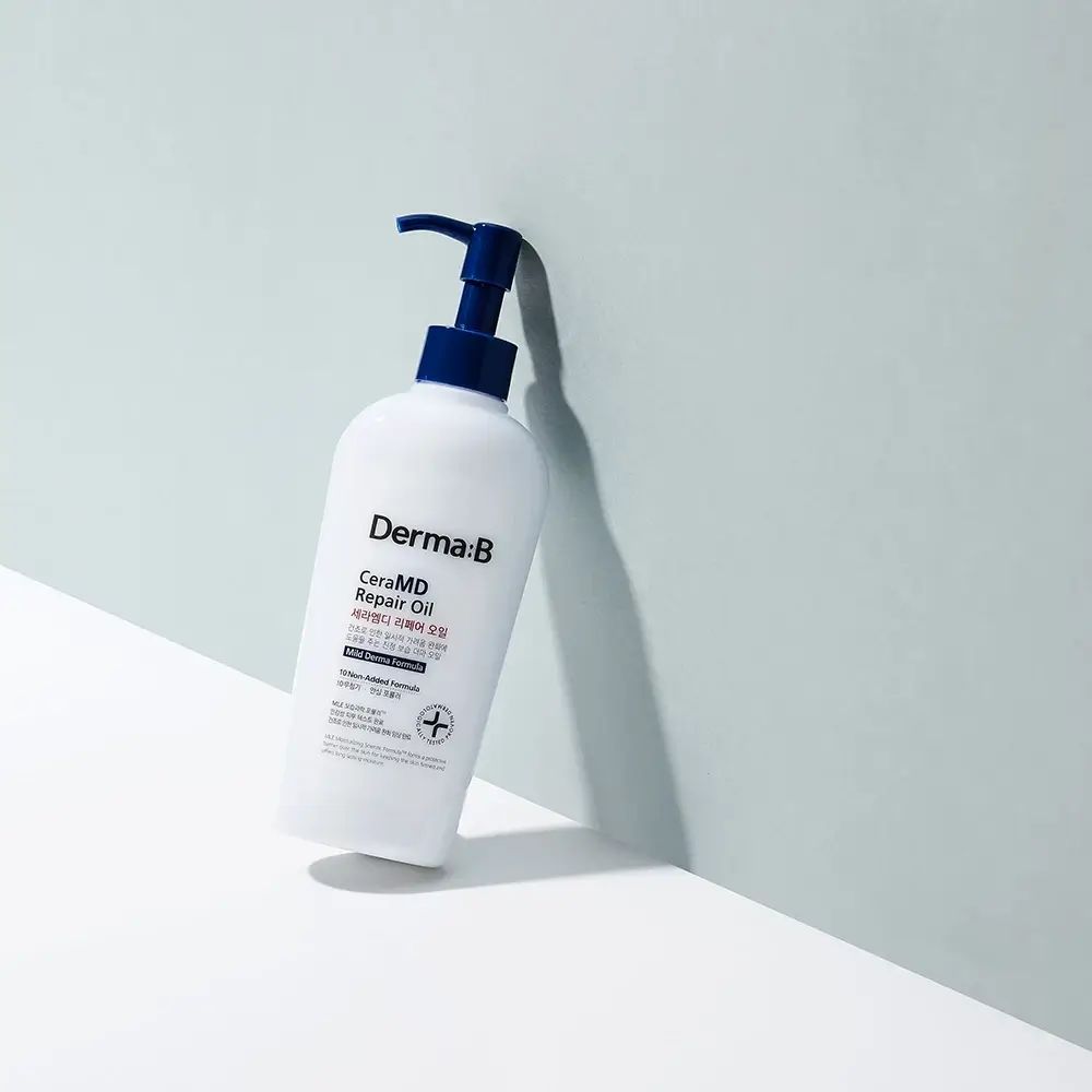 Weiße Flasche mit blauem Pumpverschluss, leicht geneigt. Aufschrift: Derma:B CeraMD Repair Oil. Hintergrund: hellblau.