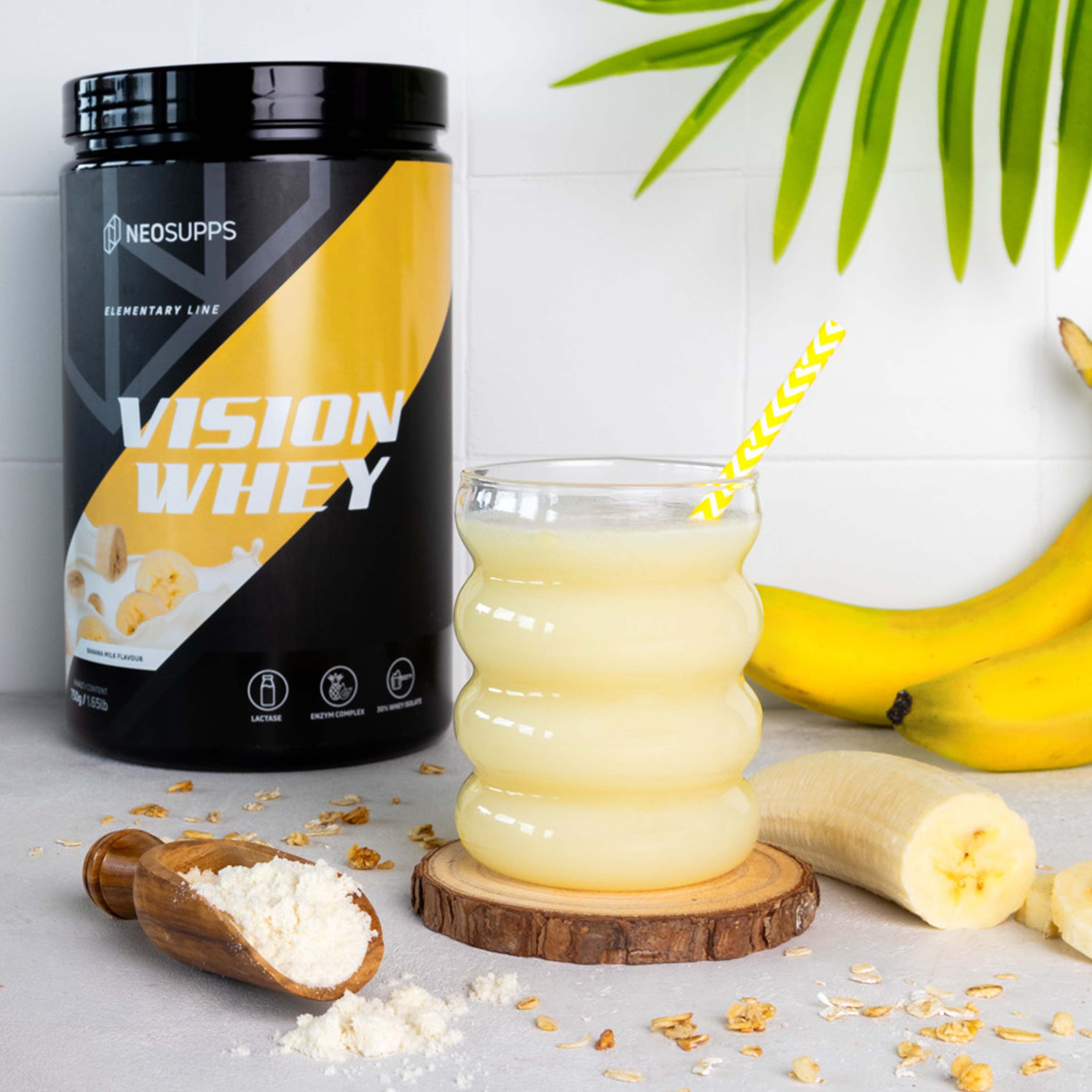 Glas mit gelbem Getränk, Strohhalm, Dose Vision Whey, Bananen, Löffel mit Pulver. Text: Vision Whey.