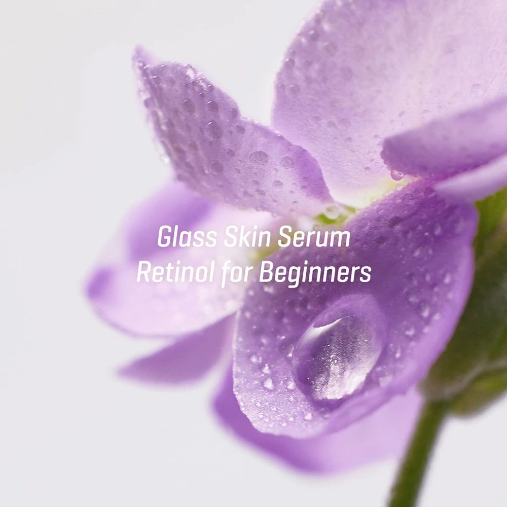 Nahaufnahme einer lila Blume mit Wassertropfen. Text: Glass Skin Serum, Retinol for Beginners.