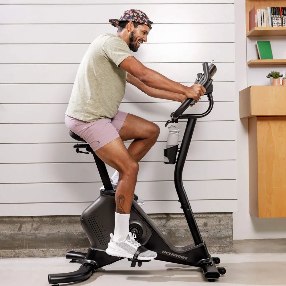 Homme faisant de l'exercice sur un vélo d'appartement. Logo Schwinn. Bouteille d'eau. Intérieur avec mur.