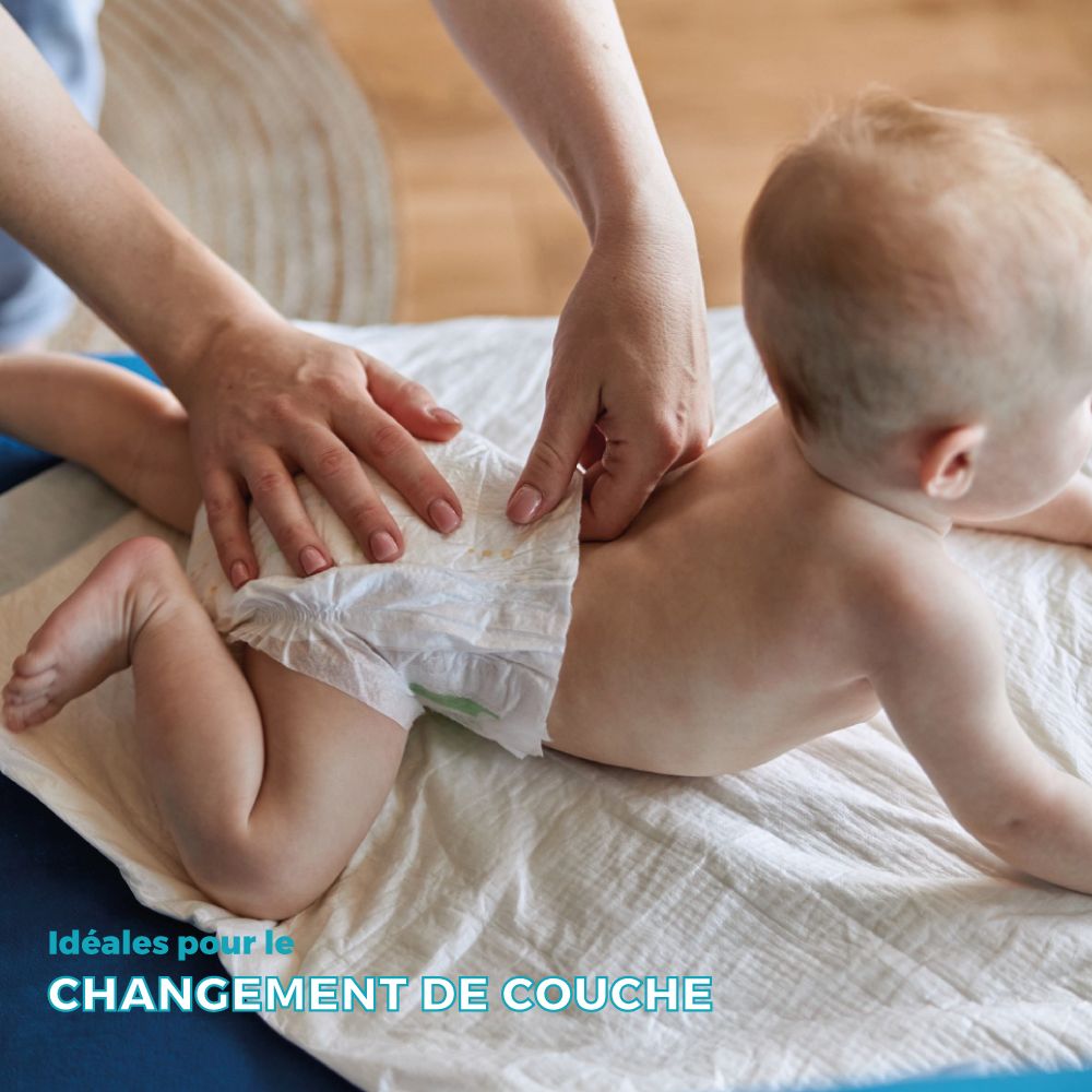 Bébé changé sur une protection de lit blanche. Mains changeant la couche. Fond bleu.