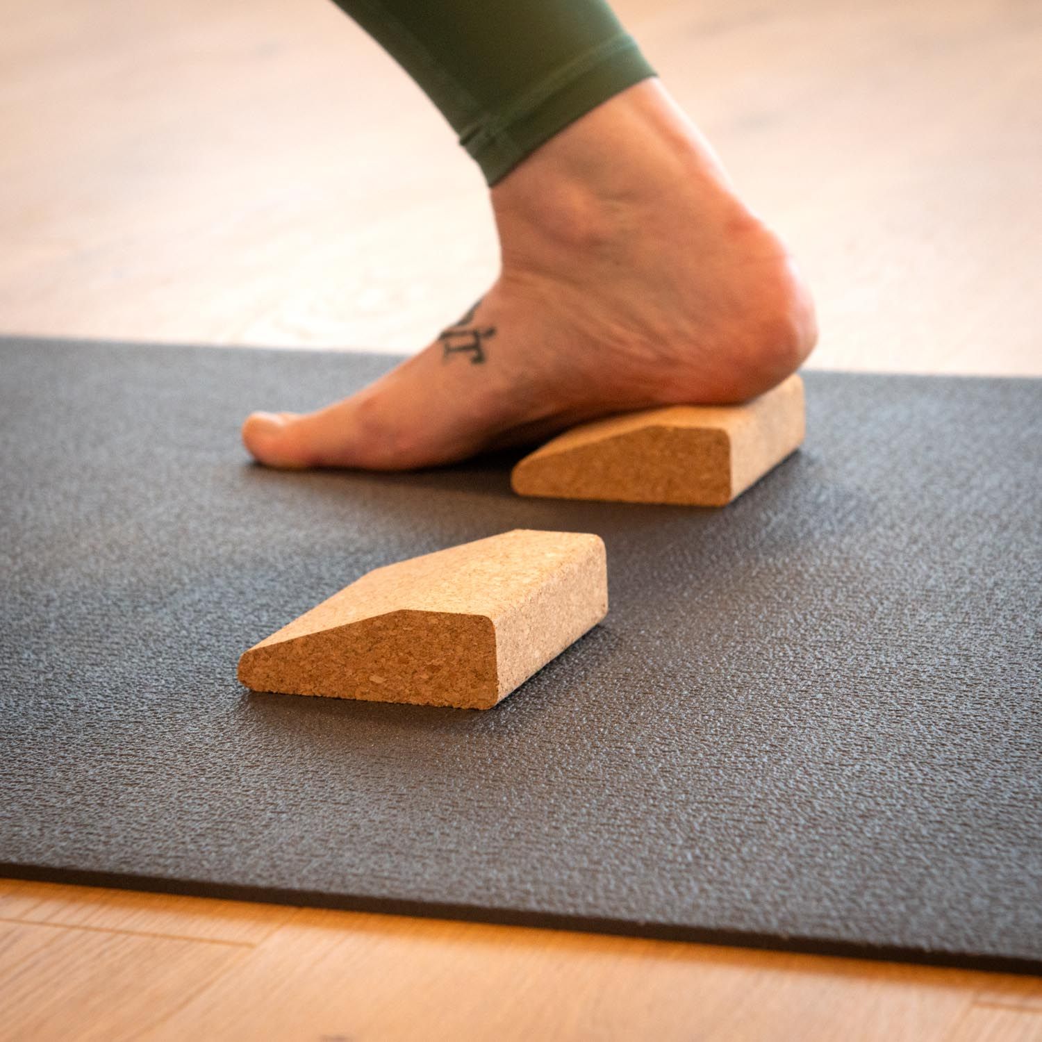 Fuß auf Korkkeil, auf Yogamatte. Zweiter Keil daneben. Helle Holzoptik im Hintergrund.