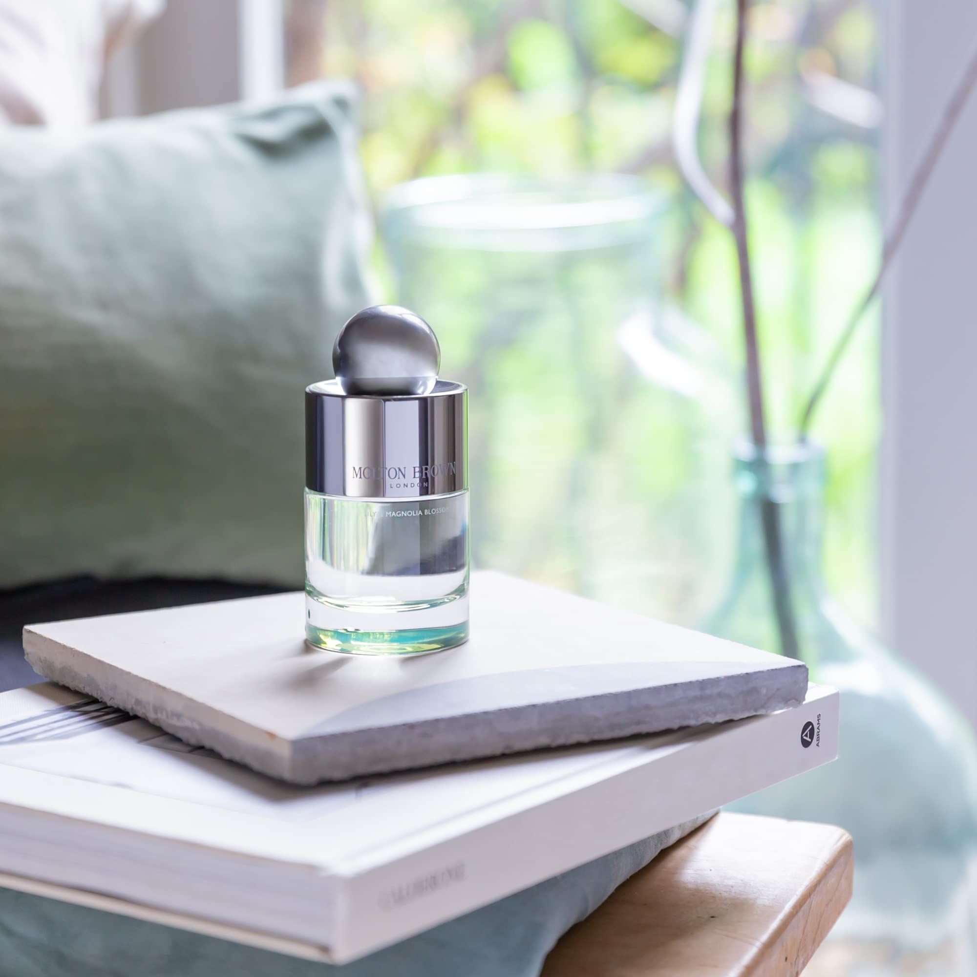 Molton Brown Lily & Magnolia Blossom Eau de Toilette auf einem Stapel Bücher. Flakon mit silberner Kappe.