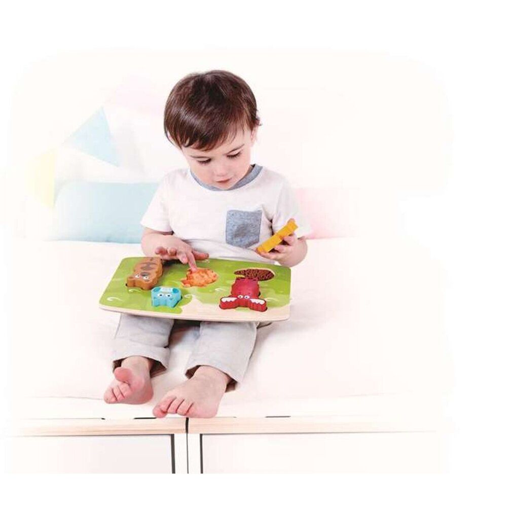 Ein Kind sitzt auf einem Bett und spielt mit einem Holzpuzzle mit Waldtieren. Das Kind hält ein Puzzleteil in der Hand.