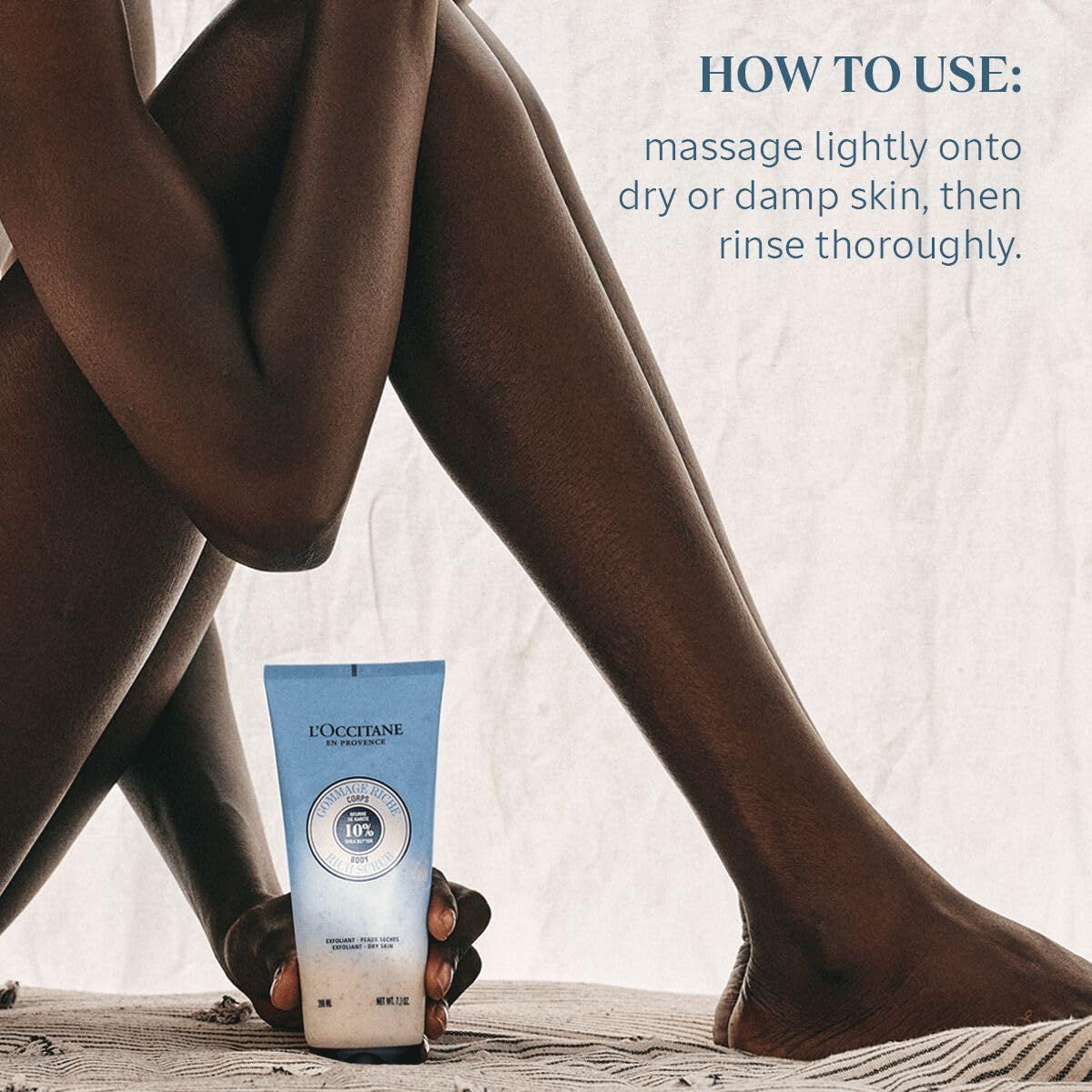Person hält Tube L'Occitane Körperpeeling. Text: HOW TO USE: massage lightly onto dry or damp skin, then rinse thoroughly.
