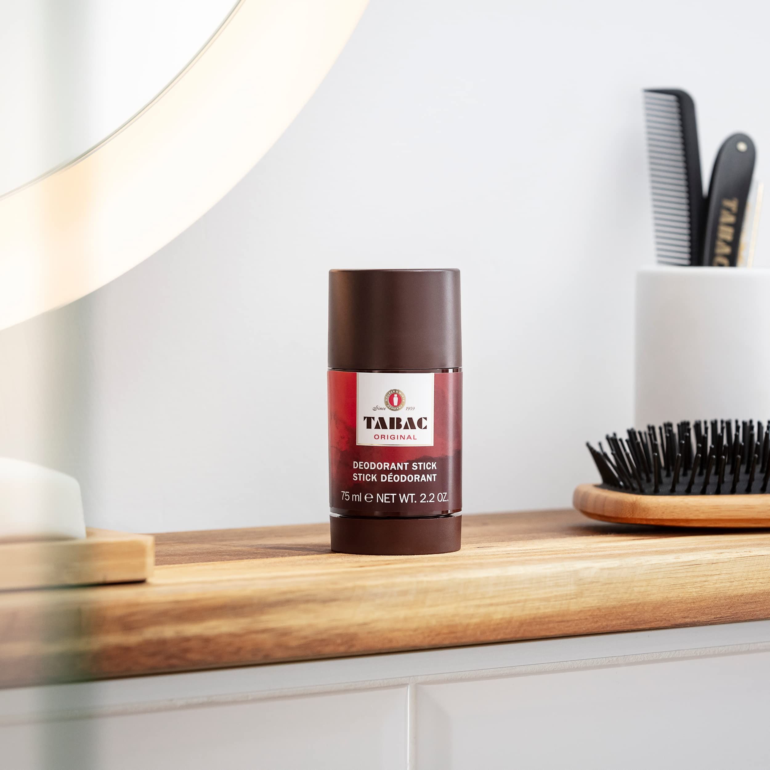 Deo-Stick Tabac Original auf Holzoberfläche. Im Hintergrund Spiegel, Kamm und Bürste. Produkt im Fokus.