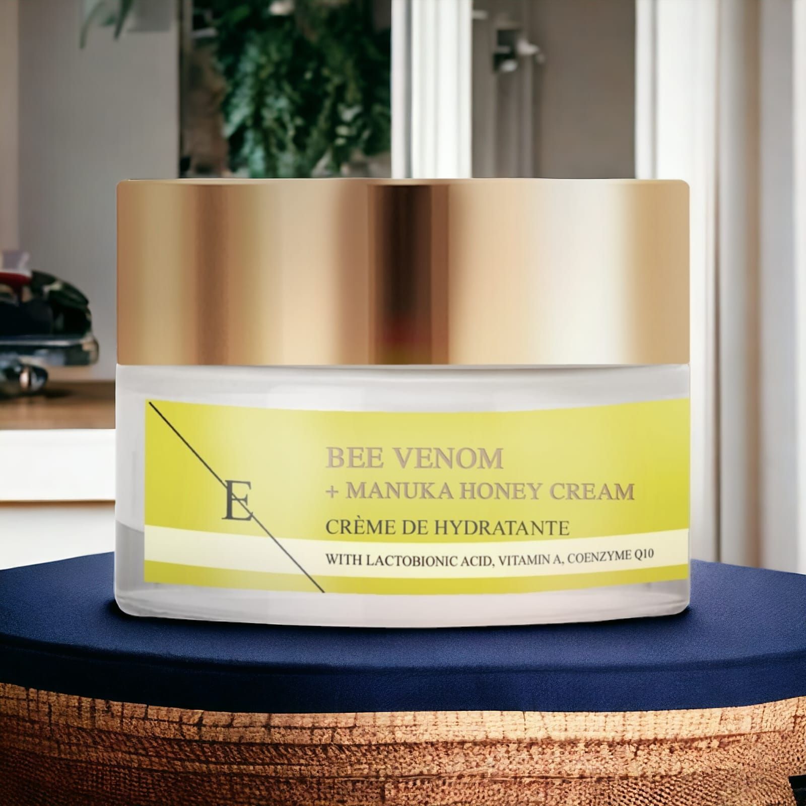 Creme-Glas mit goldfarbenem Deckel und gelbem Etikett. Aufschrift: Bee Venom + Manuka Honey Cream. Auf blauem Stoff platziert.