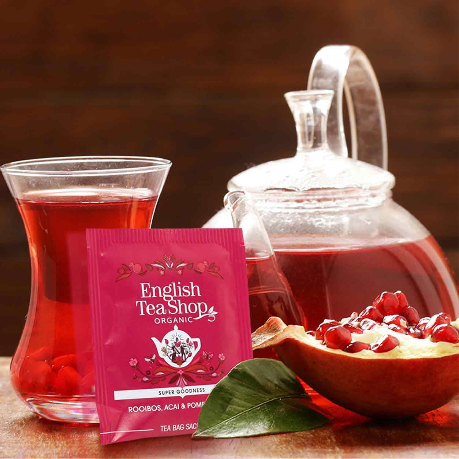 Glas mit rotem Tee, Teekanne, Teebeutel und Granatapfelhälfte. Teebeutel mit Aufschrift 'English Tea Shop'.