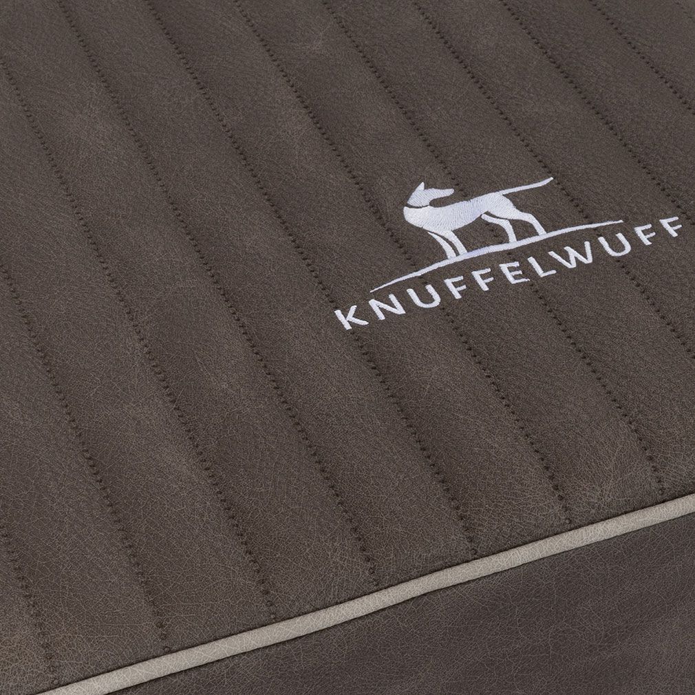 Detail der orthopädischen Hundematte. Braune Oberfläche mit vertikalen Rillen. Logo und weißer Rand.