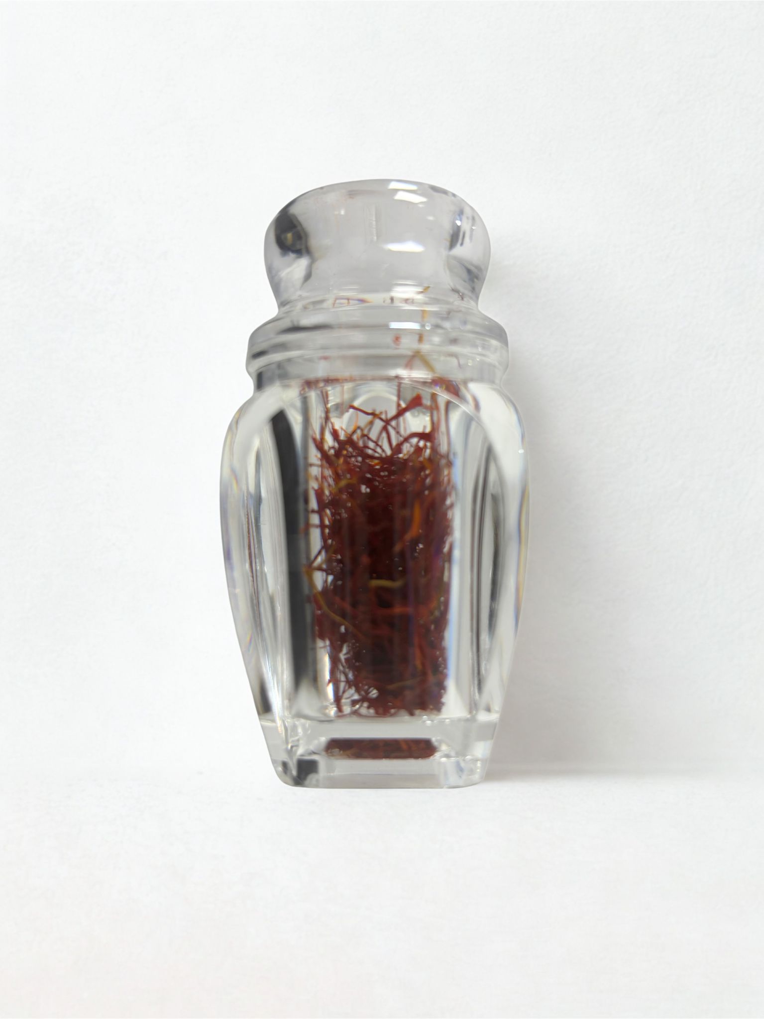 Glasbehälter mit Safranfäden. Transparenter Behälter mit Deckel. Rote Safranfäden sichtbar.