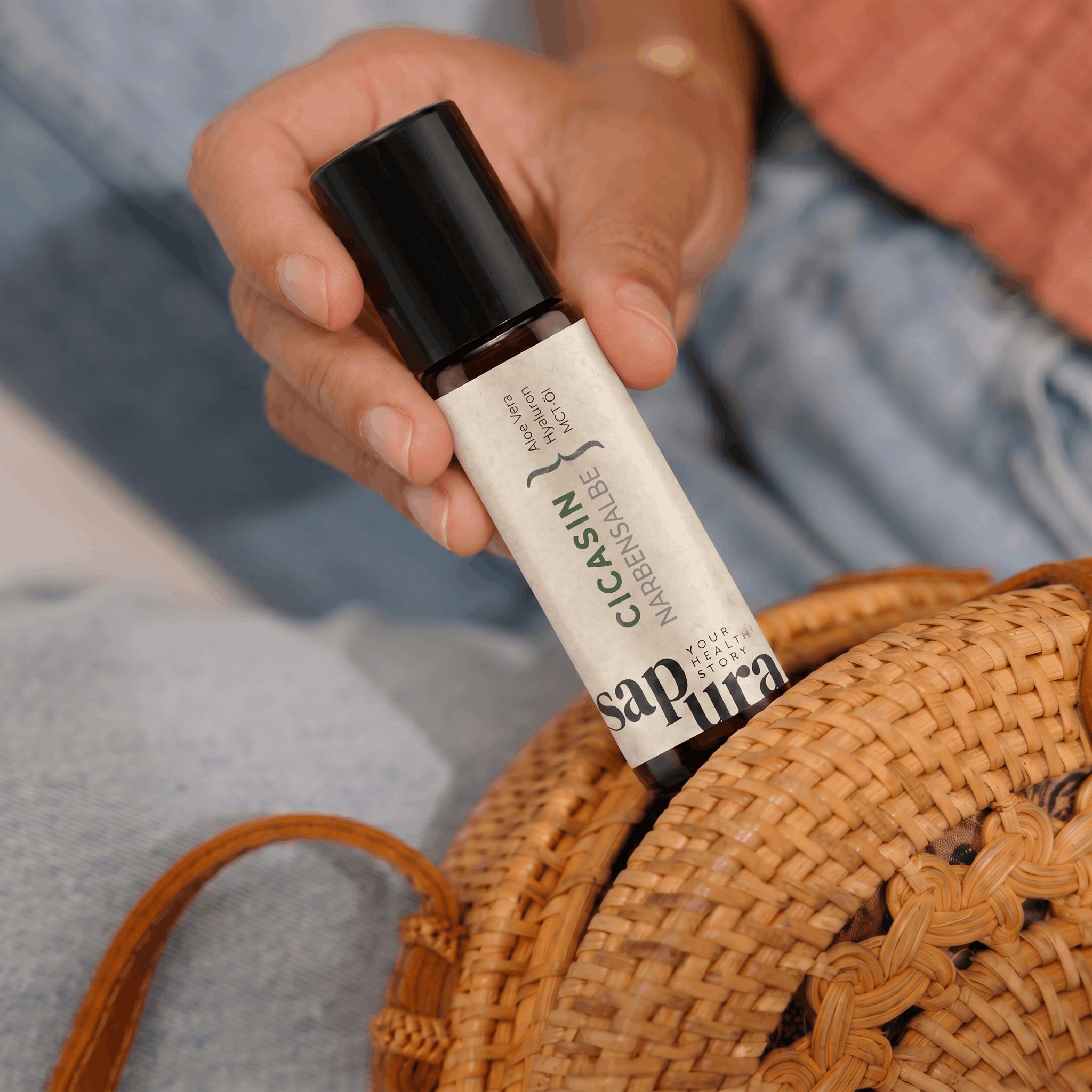 Hand hält Sapura Health CicaSin Roll-on Flasche aus einem Korb.