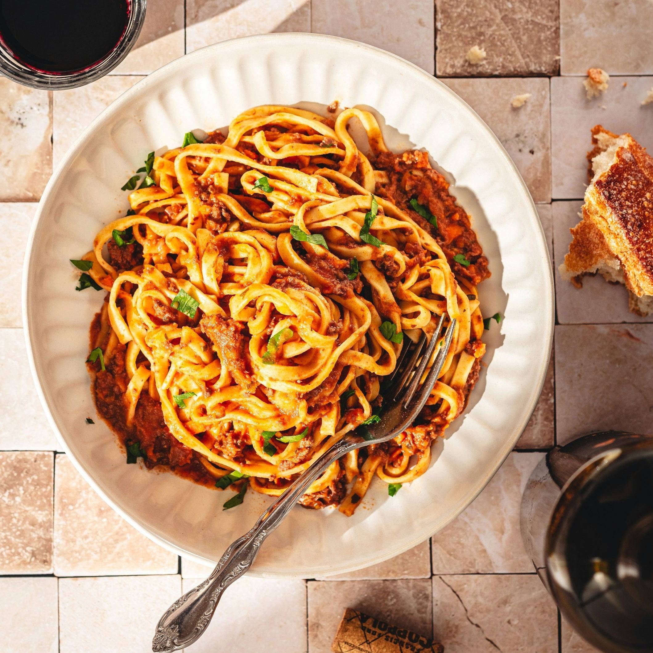 Teller mit Pasta Aglio e Olio, Gabel. Brot und Weinflasche im Hintergrund.